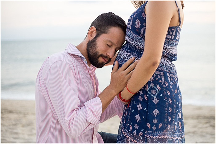 Sweet maternity photo shoot of the father holding his wifes belly on a beach