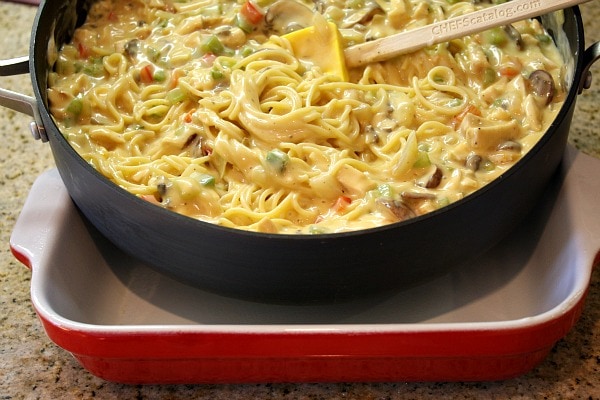 making chicken spaghetti casserole in a skillet, ready to pour it into a red and white casserole dish