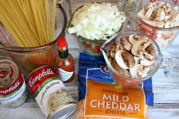 ingredients displayed for chicken spaghetti casserole- pasta, cream of mushroom soup, tabasco, cheese, onions, mushrooms, chicken
