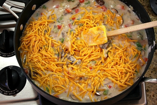 adding cheese to the sauce for chicken spaghetti casserole in a skillet